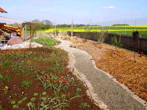 Die wassergebundene Wegedecke trennt das Blumenbeet von der mit Holzhäckseln gemulchten Hecke